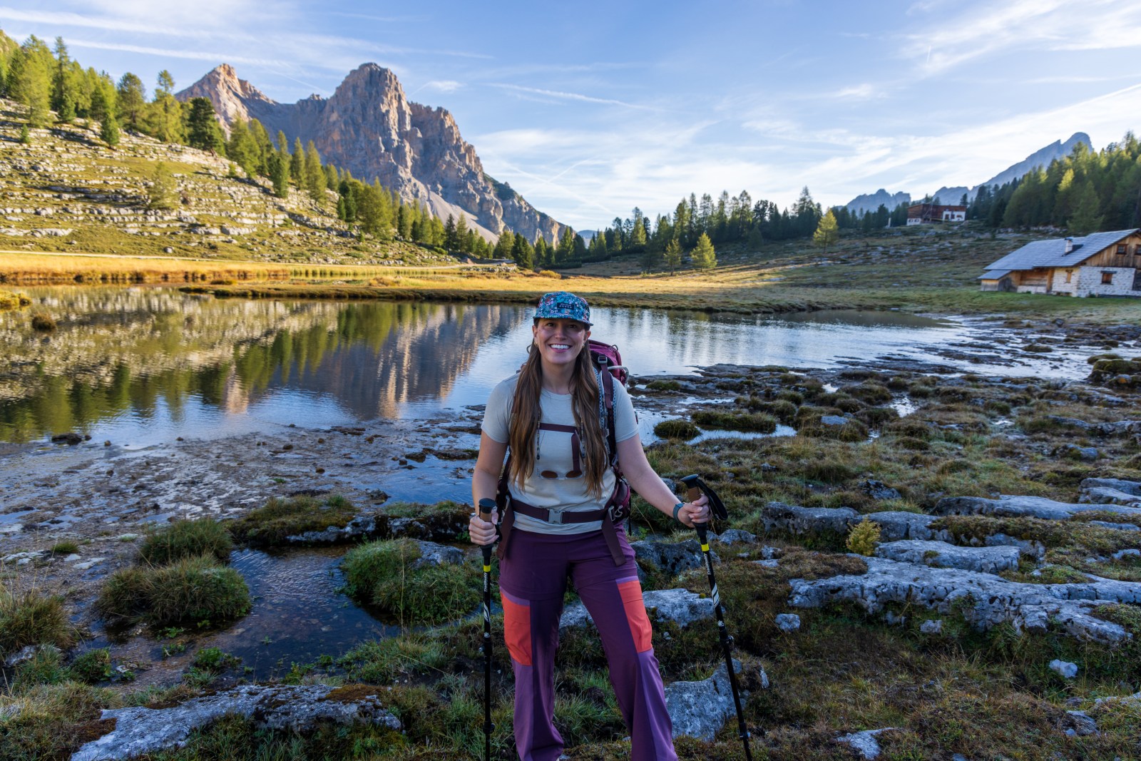 Women's hiking outfit with purple zip-off pants and trekking poles beside an alpine lake
